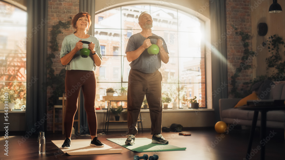Inspired Senior Couple Doing Morning Exercises and Kettlebell Workout Together at Home in Bright Living Room. Concept of Healthy Lifestyle, Fitness, Recreation, Couple Goals, Wellbeing and Retirement. Inspired Senior Couple Doing Morning Exercises and Kettlebell Workout Together at Home in Bright Living Room. Concept of Healthy Lifestyle, Fitness, Recreation, Couple Goals, Wellbeing and Retirement.