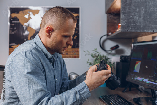 Side view of focused male video editor looking at footage on photo camera while doing post production montage at desktop computer with professional software 