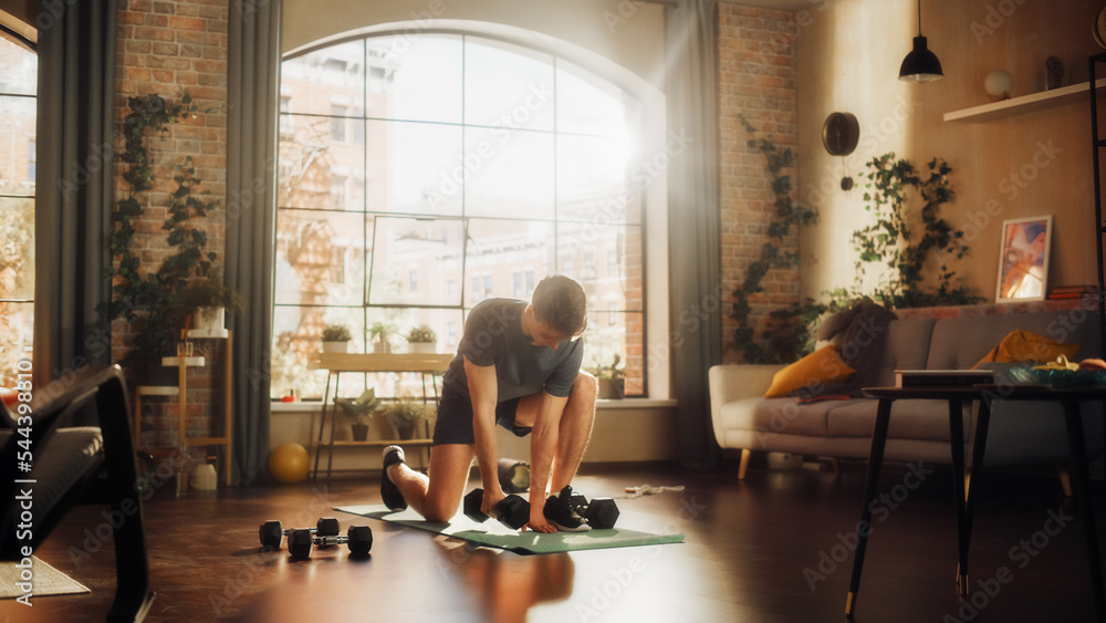 Fit Athletic Strong Young Man Training and Strengthening Arm Muscles with Dumbbell Exercises During Morning Workout at Home in Sunny Apartment. Concept of Healthy Lifestyle and Fitness. Fit Athletic Strong Young Man Training and Strengthening Arm Muscles with Dumbbell Exercises During Morning Workout at Home in Sunny Apartment. Concept of Healthy Lifestyle and Fitness.