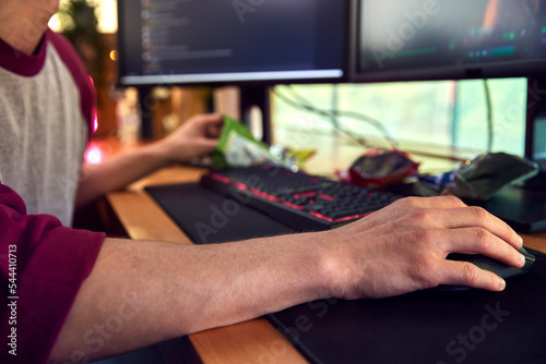 Close Up Of Man Gaming At Home Eating Potato Chips Sitting At Desk With Monitors