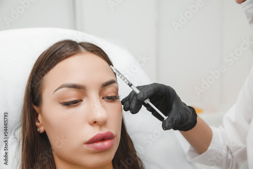A cosmetologist makes anti-aging injections against wrinkles on the forehead on the face of a beautiful woman. Women's aesthetic cosmetology in a beauty salon.