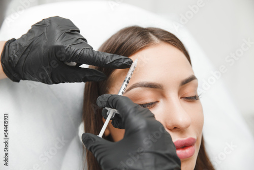 A cosmetologist makes anti-aging injections against wrinkles on the forehead on the face of a beautiful woman. Women's aesthetic cosmetology in a beauty salon.