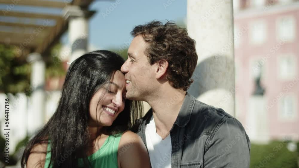 Closeup of beautiful multiracial couple enjoying sunny day outside. Handsome Caucasian man kissing his girlfriends forehead and pointing at something in distance. Lifestyle, relationship concept. Closeup of beautiful multiracial couple enjoying sunny day outside. Handsome Caucasian man kissing his girlfriends forehead and pointing at something in distance. Lifestyle, relationship concept.