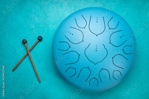 blue steel tongue drum with mallets, top view against textured paper background