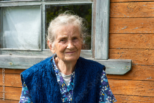 Portrait of an old peasant woman sitting near a village house.