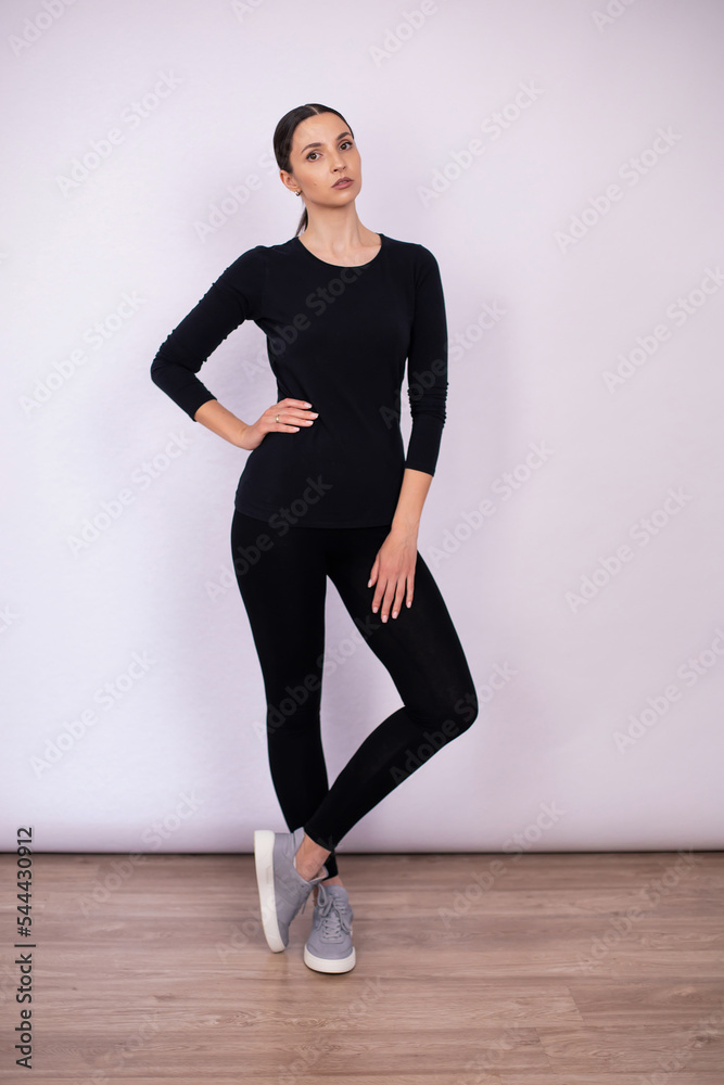 full length woman poses in black tight fitting clothes and sneakers in a studio on a white background.