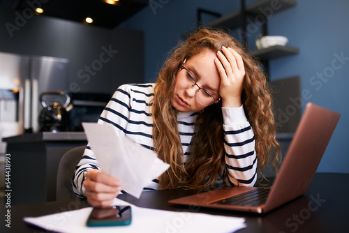 Unhappy woman calculates expenses on bills, upset about increased utilities prices. Female counting paychecks, debts, loans, reciepts to pay taxes. Inflation, financial crisis, low paying capacity.