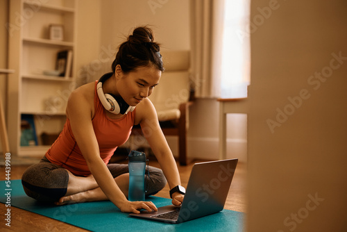 Fototapeta Young Asian athletic woman surfing the net on laptop at home.