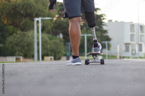 Back view of man with disability skating on sunny day. Strong person in casual clothes with prosthetic leg on skateboard. Sport, disability, hobby concept