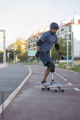 Man with mechanical leg in casual clothes skateboarding. Mid adult sportsman riding down special road in concentration. Sport, disability, training concept