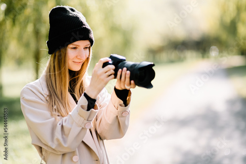 young beautiful girl is resting in nature with camera. woman photographer walking in the park on an autumn day © Pavel