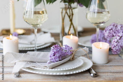 Beautiful table decor for a wedding dinner with a spring blooming lilac flowers. Celebration of a special event. Fancy white plates  wineglasses  candles. Countryside style