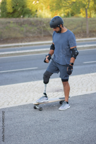Determined person with disability learning skateboarding. Caucasian man with mechanical leg in helmet in park on sunny day, trying to skateboard. Sport, disability concept