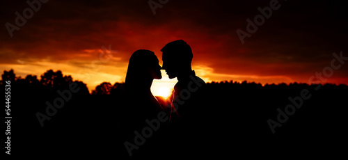 Silhouette of a young couple in love face to face against the background of the orange sky during sunset.