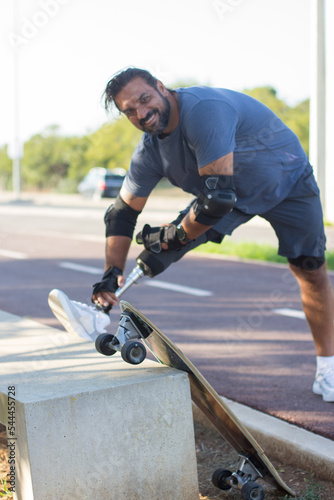Portrait of dark-haired Caucasian man with skateboard. Mid adult sportsman in casual clothes and equipment looking at camera, smiling. Sport, lifestyle, training concept