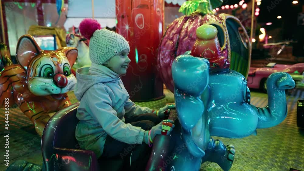 Cute little girl is riding an elephant on a merry-go-round carousel in the amusement park at night