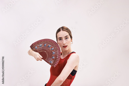 A girl in a red top and a black skirt with a fan in her hands dances a passionate Spanish flamenco dance. Artistic movements, emotions, the ability to keep yourself on stage. A charming woman.