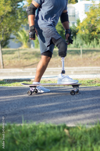 Side view of skater with prosthetic leg. Man with disability riding black longboard on sunny summer day. Sport, extreme, determination concept