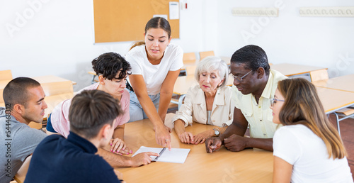Принти на полотні Portrait of young emotional girl participating adult education class with mixed age group of women and men of different nationalities, discussing learning material around table in classroom