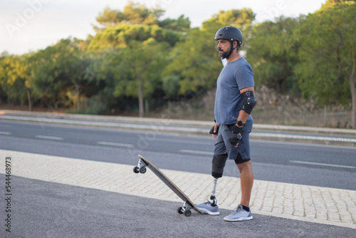 Side view of determined person with disability on skateboard. Caucasian man with mechanical leg in helmet skateboarding in park on sunny day. Sport, disability concept