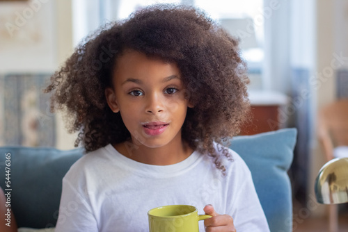 Portrait of African American girl with yellow mug. Cute child with curly hair drinking hot cocoa milk. Portrait, childhood concept