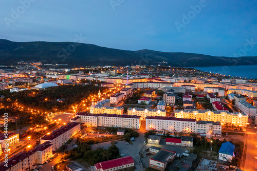 Night aerial photograph of a seaside port town. Top view of illuminated streets and buildings. Mountains and sea in the distance. City of Magadan, Magadan region, Far East of Russia.