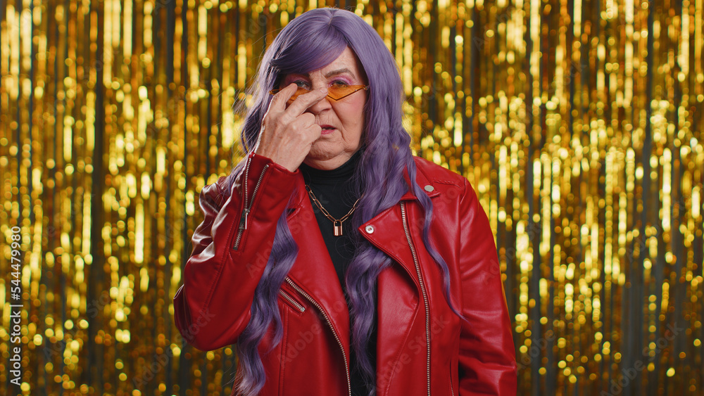 I am watching you. Woman with purple hairstyle wig pointing at his eyes and camera, show I am watching you gesture, spying on someone. Senior elderly grandmother on shiny disco party foil background I am watching you. Woman with purple hairstyle wig pointing at his eyes and camera, show I am watching you gesture, spying on someone. Senior elderly grandmother on shiny disco party foil background