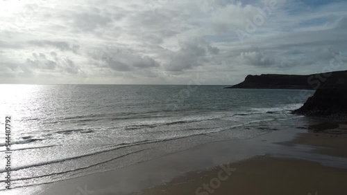 Gentle Sea Waves on Mewslade Bay with Dramatic Cloudy Sky and Coastal Mountains in Gower Peninsula Wales UK - 4K Aerial Drone Shot photo