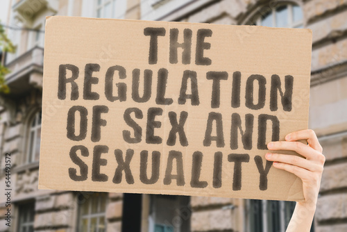 The phrase " The regulation of sex and sexuality " is on a banner in men's hands with blurred background. Adult. Immoral. No Sex. Abuse. Authority. Gender. Behavior. Crime. Equality. Flirting © AndriiKoval