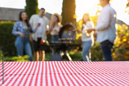 Empty table and blurred view of friends having barbecue party outdoors. Space for text