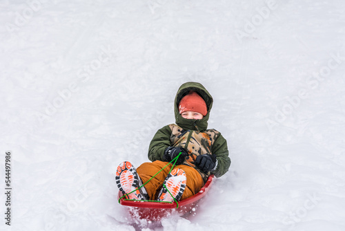 The boy slides from the snowy hill on a speedy sled