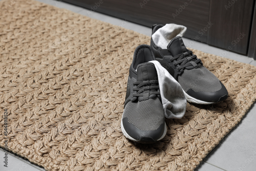 Sneakers with dirty socks on woven mat indoors, closeup. Space for text Sneakers with dirty socks on woven mat indoors, closeup. Space for text