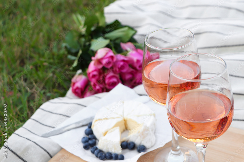 Glasses of delicious rose wine, flowers and food on picnic blanket outdoors Glasses of delicious rose wine, flowers and food on picnic blanket outdoors