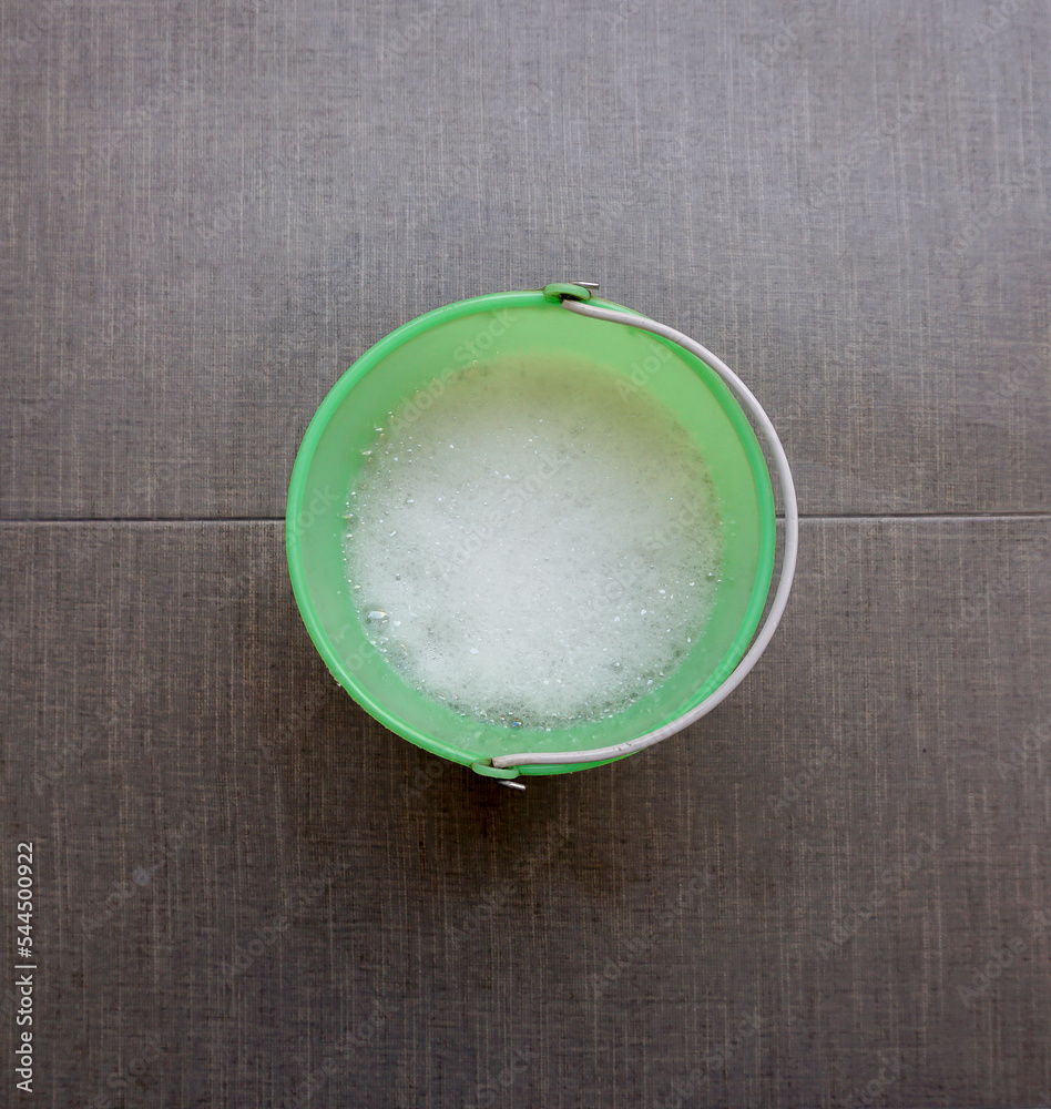green plastic container with sparkling water that will be used for cleaning. the background is gray with texture green plastic container with sparkling water that will be used for cleaning. the background is gray with texture
