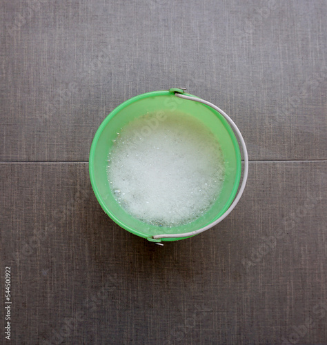 green plastic container with sparkling water that will be used for cleaning. the background is gray with texture
