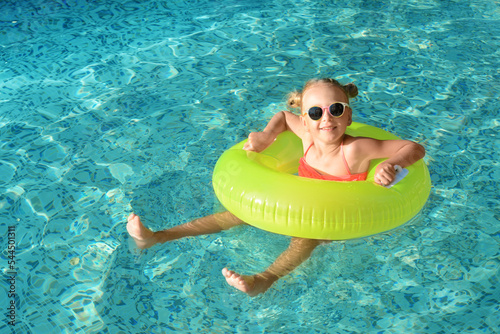 Fotografie Happy little girl with inflatable ring in outdoor swimming pool on sunny day