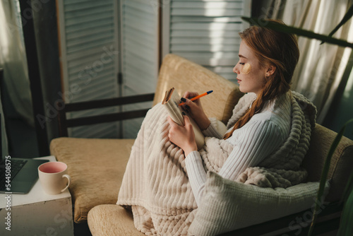 Fotografia Cute lady with eyes patches at home writing notes on a diary while relaxing taking a break, enjoying home lifestyle