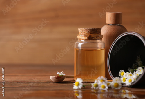 Chamomile essential oil and flowers on wooden table, space for text