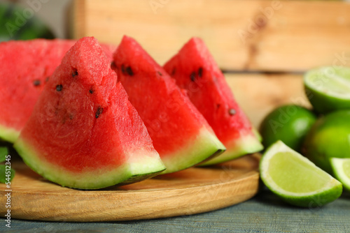 Slices of delicious watermelon and limes on light blue wooden table, closeup