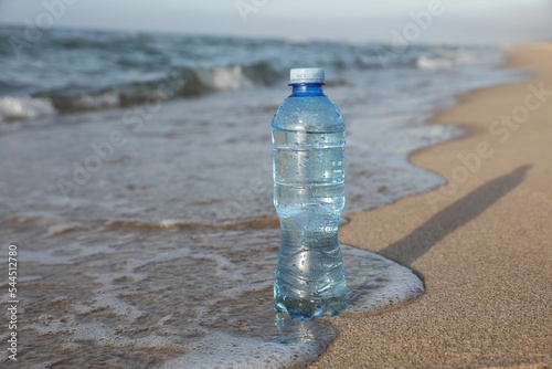 Plastic bottle of fresh water on wet sand near sea