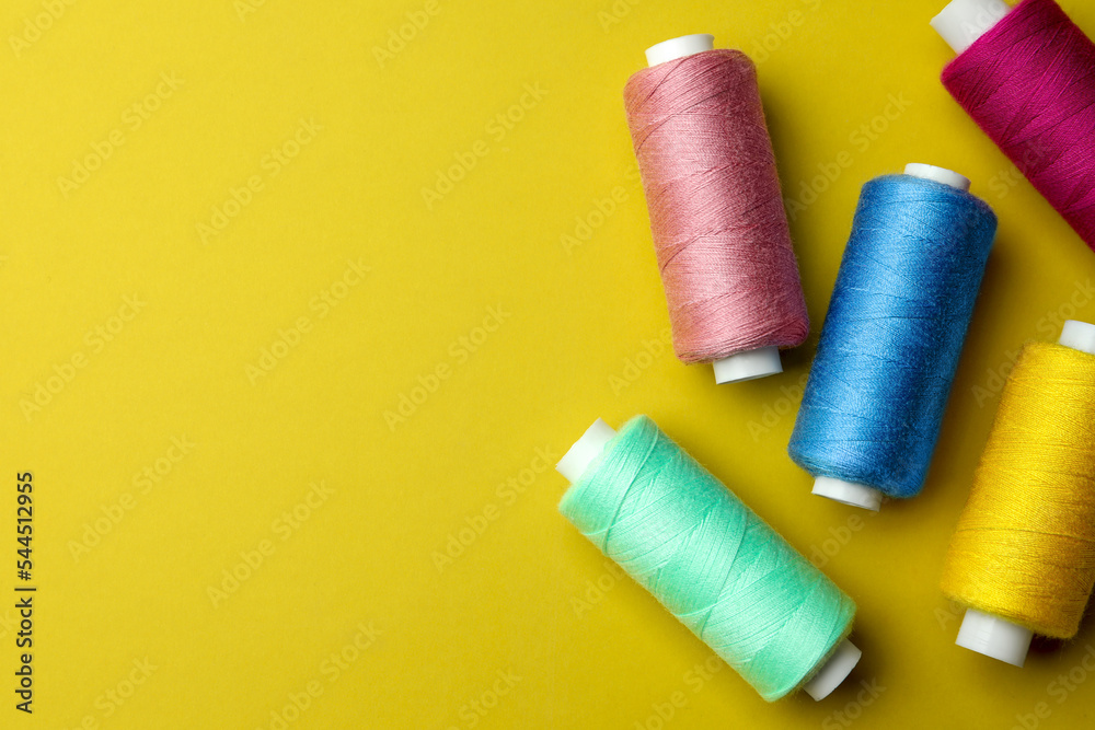 Different colorful sewing threads on yellow background, flat lay. Space for text Different colorful sewing threads on yellow background, flat lay. Space for text
