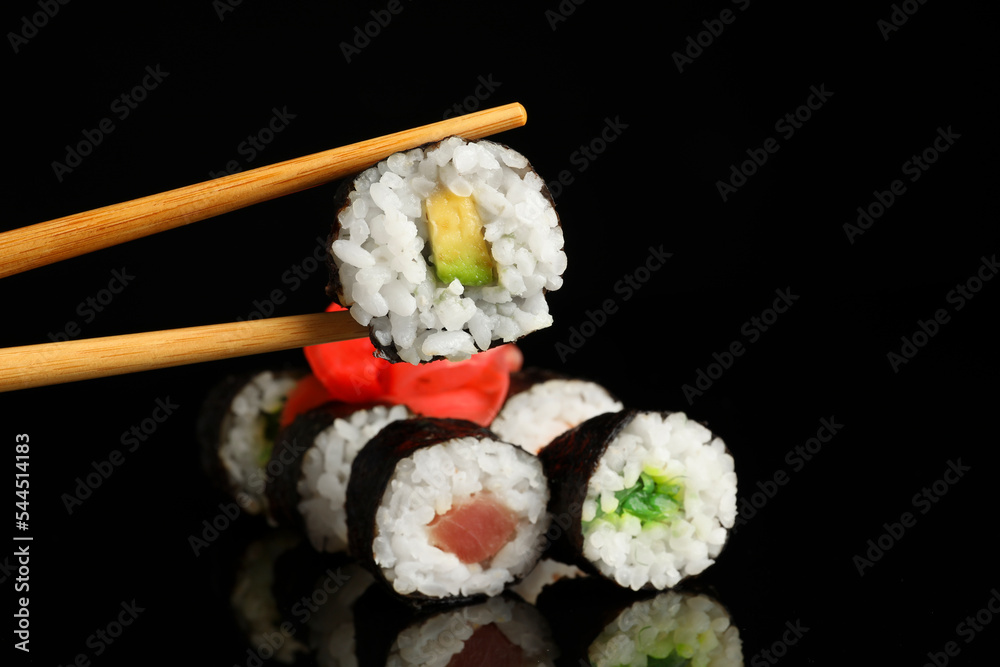 Set of delicious sushi rolls and chopsticks on black background Set of delicious sushi rolls and chopsticks on black background