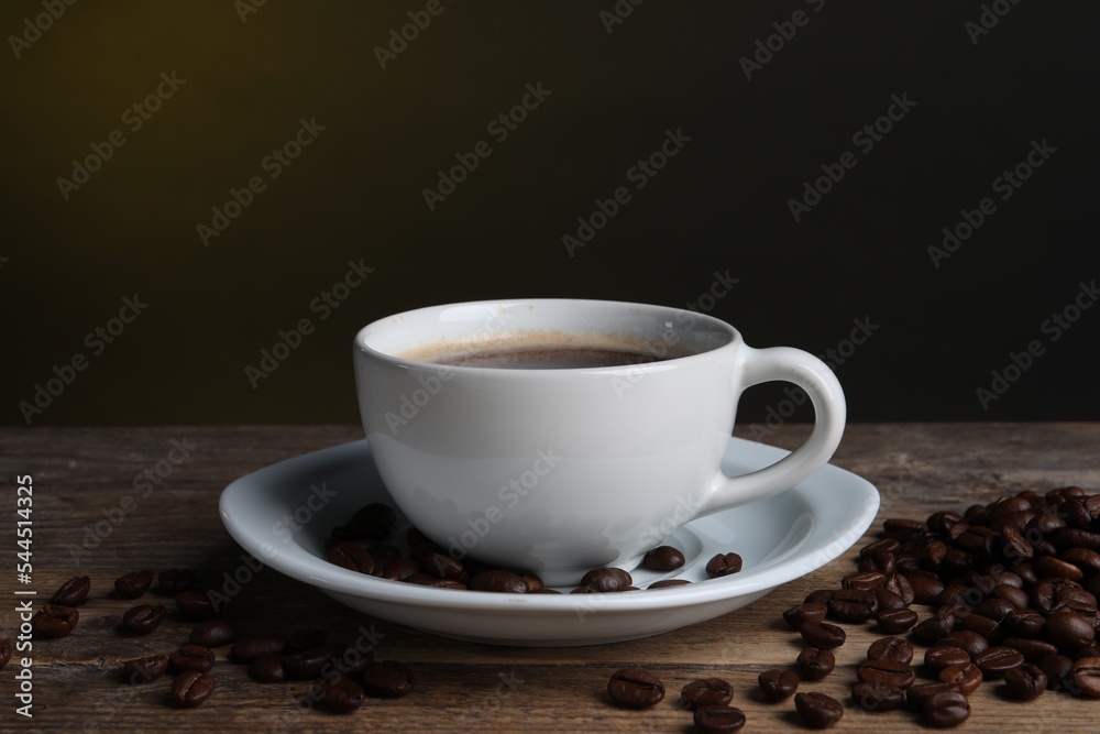 Cup of hot aromatic coffee and roasted beans on wooden table against dark background Cup of hot aromatic coffee and roasted beans on wooden table against dark background