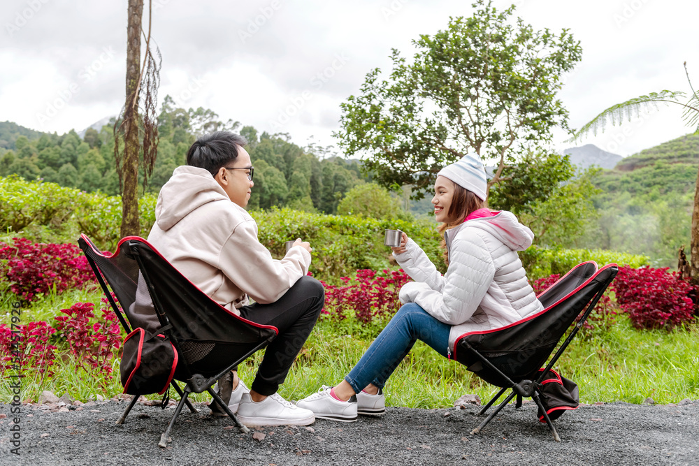 Asian couple sitting while holding hot drink enjoying camp activity Asian couple sitting while holding hot drink enjoying camp activity