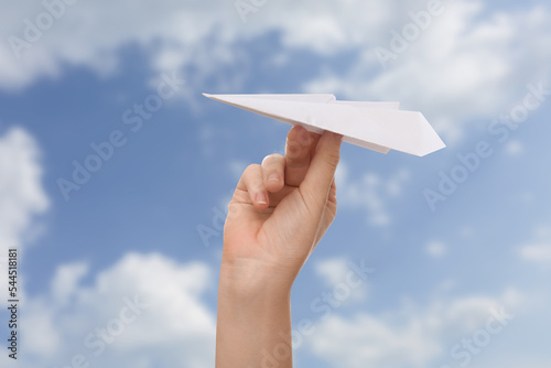 Female hand holding paper plane against blue sky