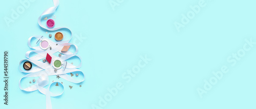 Christmas tree made of makeup products, Christmas decorations and ribbon on light blue background with space for text