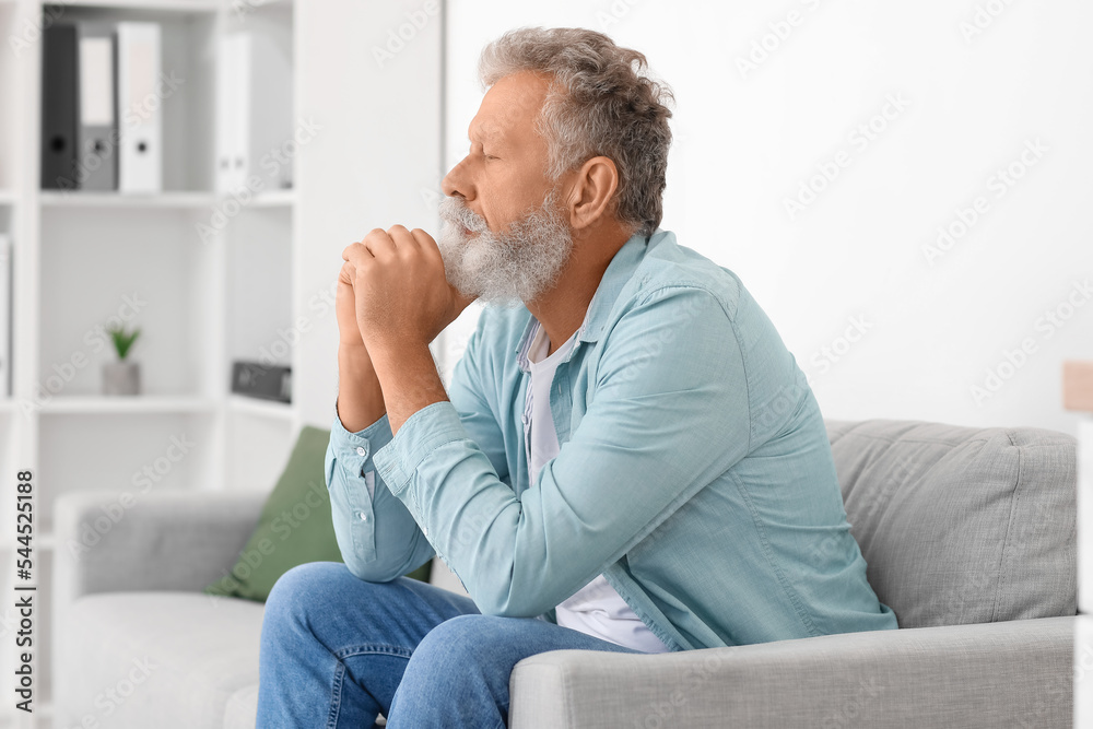Thoughtful senior man sitting on sofa at home