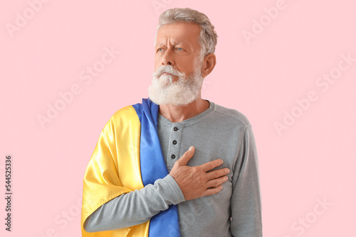 Mature man with flag of Ukraine praying on pink background