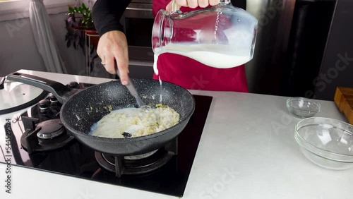 Chef cook making white cheese sauce for mac and cheese meal. Ingredients: Milk, cheese, flour and butter in wok pan on kitchen gas stove.
