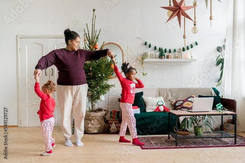 Happy African American family having fun and celebrating Christmas holidays indoor. Cheerful pregant mother and two daughters dancing together at home